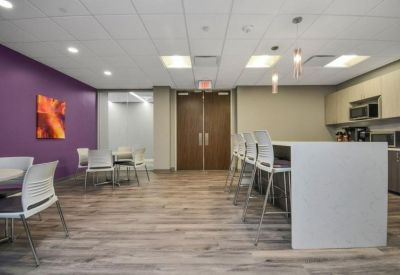 Modern breakroom featuring a white island, purple accent wall, and a small kitchenette.
