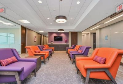 Vibrant lounge area featuring rows of orange and purple armchairs and a wall-mounted TV.