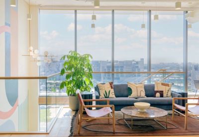 Sunny lounge area with a blue sofa, colorful pillows, and large windows overlooking the city.