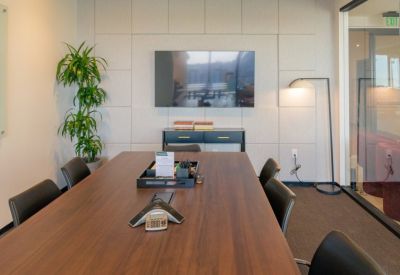 Professional meeting room featuring a long wooden table, black chairs, and a large wall-mounted screen.