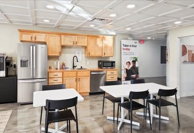 Communal kitchen area with light wood cabinets, stainless steel appliances, and café seating.