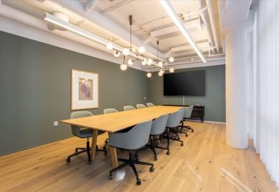 Professional boardroom with a long light-wood table, teal chairs, and a large wall-mounted screen.