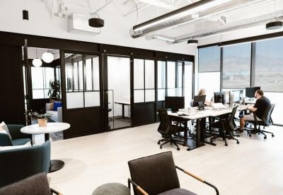 Bright common area with lounge seating, glass-walled meeting rooms, and large windows.