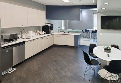 Bright office kitchen with white cabinetry, coffee station, and a dining table.