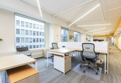 Open-plan office with L-shaped desks, ergonomic chairs, and large windows.