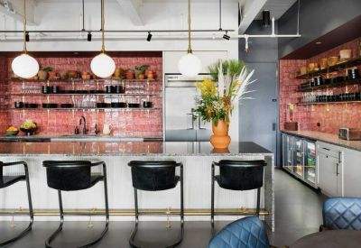 Modern communal kitchen with a marble island, pink tiled backsplash, and hanging globe lights.