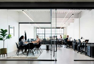 Bright, glass-walled office space with several people working at desks and a central meeting table.