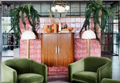 Cozy lounge area featuring green velvet armchairs and a pink tiled feature wall with hanging plants.