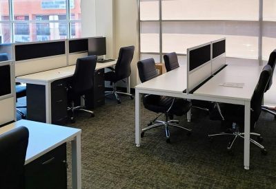 Modern office workspace featuring white desks with privacy dividers and black chairs.
