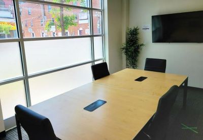 Professional meeting room with a wooden table, black chairs, and a wall-mounted screen.