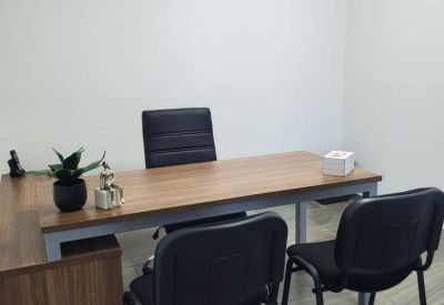 Private office with a light wood desk, black chairs, and a small potted plant.