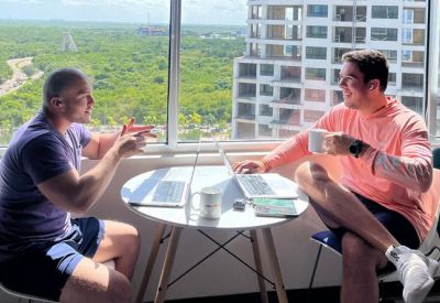 Two men having a casual meeting at a round white table overlooking a lush green area.