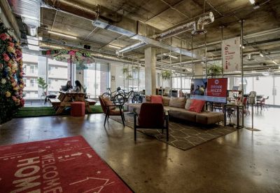Spacious communal lounge with industrial ceilings, a sofa area, and a picnic table under a floral umbrella.