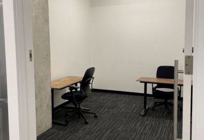 Private two-person office suite with wooden desks, ergonomic chairs, and grey carpet.