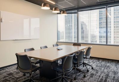 Bright boardroom with a large wooden table, black mesh chairs, and a whiteboard.