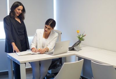 Two professionals collaborating at a white desk with a laptop and notebook.