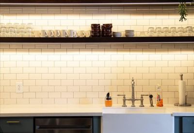 Modern communal kitchen with dark teal cabinetry, subway tile, and checkerboard floor.