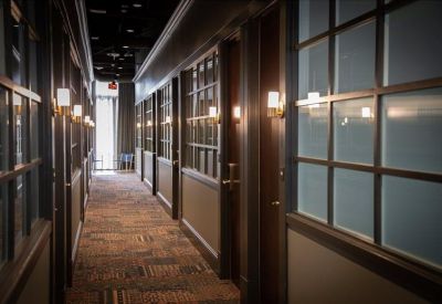 Long office corridor with glass-partitioned private suites and patterned carpet.
