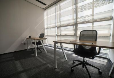 Private two-person office suite with light wood desks and mesh chairs by a large window.