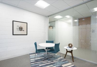 Small breakout room with a circular table, blue chairs, and a glass partition wall.
