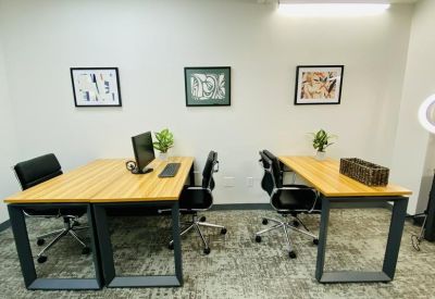 Open office area featuring two light wood desks with ergonomic black chairs and abstract wall art.