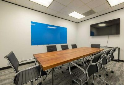 Conference room featuring a wooden table, blue chairs, and a large digital screen.