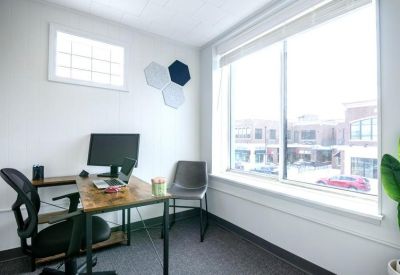 Bright private office with a desk, monitor, and large window overlooking the street.