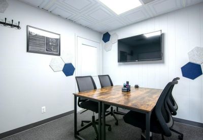 Meeting room with a wooden table, wall-mounted TV, and geometric acoustic panels.