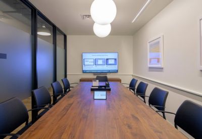 Professional boardroom with a long wooden table, blue chairs, and video conferencing equipment.
