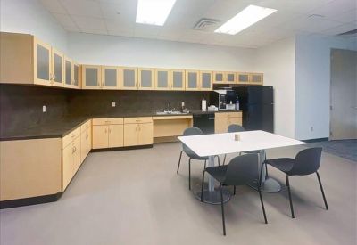Modern office kitchen and breakroom with light wood cabinetry and a dining table.