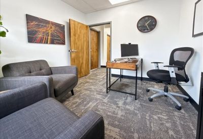 Private office suite with a desk, ergonomic chair, and grey guest sofa.