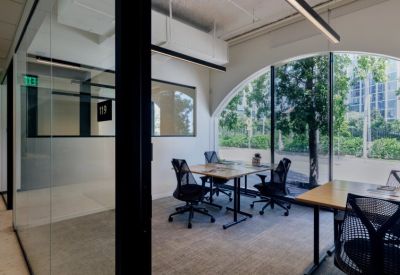 Bright private office featuring a wooden desk, ergonomic chairs, and a large arched window overlooking trees.
