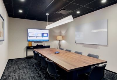 Professional boardroom with a large wood table, comfortable black chairs, a wall-mounted TV, and a whiteboard.