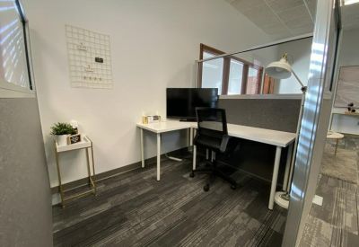 Modern private office with a white L-shaped desk and black mesh chair.