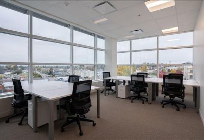 Bright open-plan office with white desks, black ergonomic chairs, and large windows.