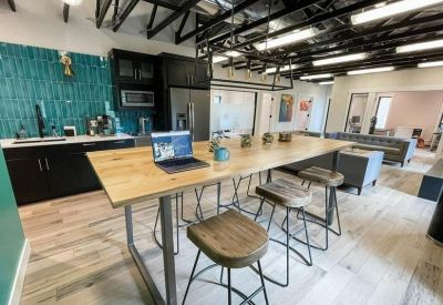 Modern communal kitchen and breakout area with a blue tiled backsplash and high-top wood table.