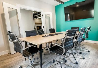 Light-filled meeting room featuring a wooden table, black ergonomic chairs, and a teal accent wall.