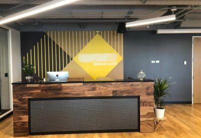 Reception desk crafted from natural wood with a geometric yellow and charcoal feature wall.