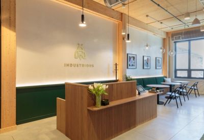 Timber-slatted reception desk with a gold bee logo and green velvet banquette seating.