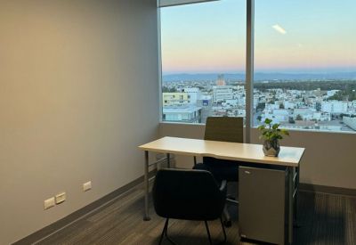 Private office suite with a desk, two chairs, and a large window overlooking the city at sunset.