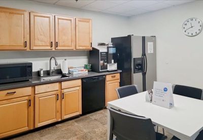 Modern breakroom kitchen with wooden cabinets, stainless steel refrigerator, and a small dining table.