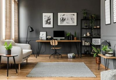 Stylish communal lounge area with a grey sofa, wooden desk, indoor plants, and grey walls.