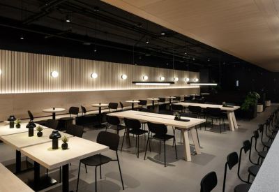 Spacious communal dining area with long white tables, black chairs, and modern wall lighting.