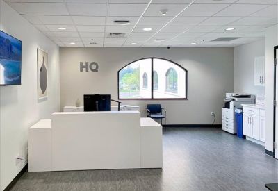 Bright reception area with a white front desk and arched window under a high ceiling.