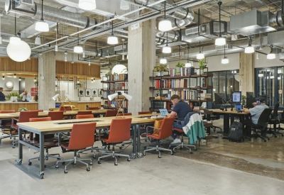 Open-plan coworking space with long wooden tables and rows of orange task chairs.