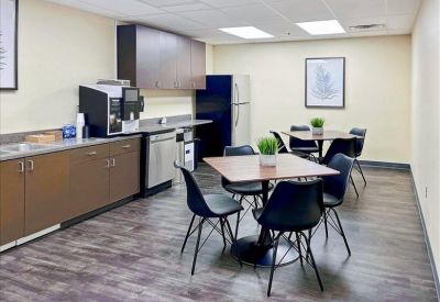 Modern breakroom kitchen with a coffee station, dining tables, and full-sized refrigerator.