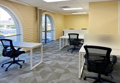 Coworking space with white desks, ergonomic chairs, and large arched windows.