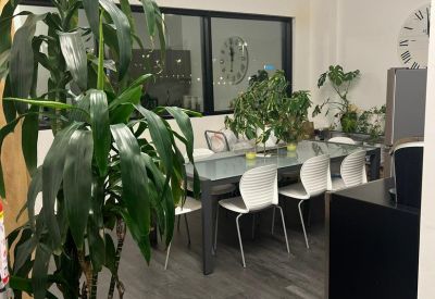 Communal break area with a long glass-top table, white chairs, and indoor plants.