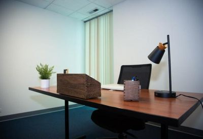 Private office featuring a wooden desk with a black lamp, laptop, and small potted plant.