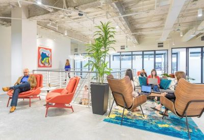 Bright coworking lounge with mid-century modern armchairs, a large potted plant, and colorful abstract art.
